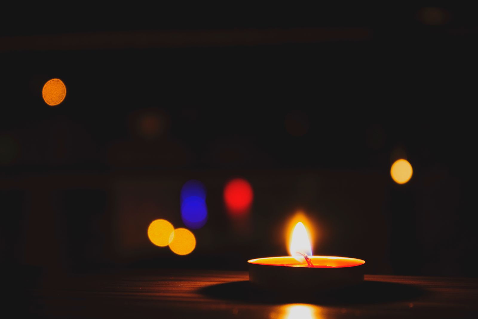 Bougie chauffe-plat allumée avec des lumières bokeh colorées dans le noir
